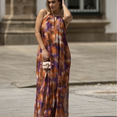 Vestido comprido com padrão colorido abstrato e mala bege em cenário urbano