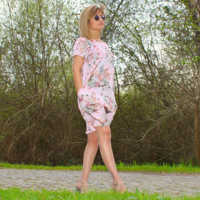 Mulher com conjunto floral cor-de-rosa e óculos de sol a caminhar em caminho de pedra e árvores ao fundo