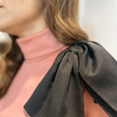 Acessório de tecido preto com pregas sobre ombro de camisa rosa de gola alta