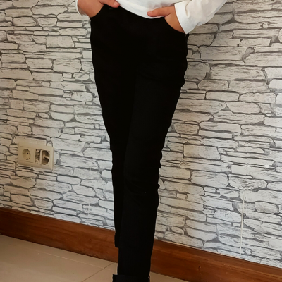 Calça preta justa com fundo de parede de pedras claras