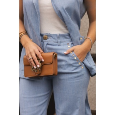 Conjunto azul claro com mala castanha pequena e acessórios em fundo neutro.