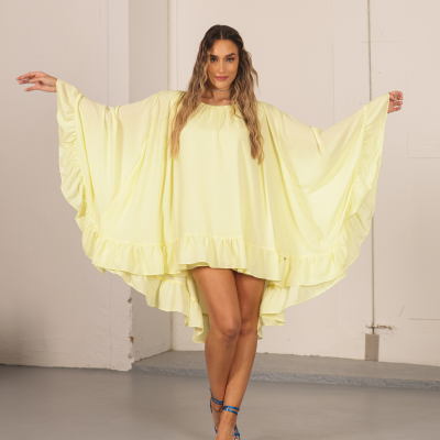 Vestido amarelo claro com mangas amplas e folhos usado por mulher com sandálias azuis em ambiente interior.