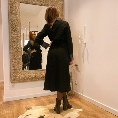 Casaco preto comprido com detalhes azuis e botas castanhas em frente a espelho grande com moldura decorada