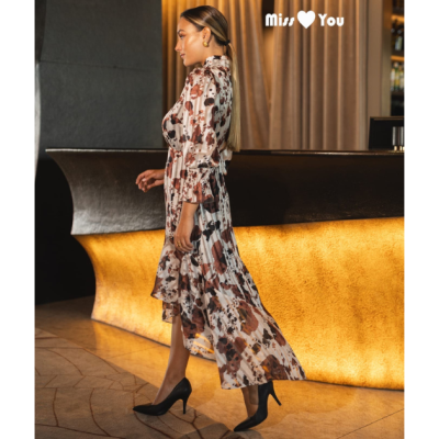 Mulher de perfil usando vestido floral longo e sapatos de salto em bar iluminado