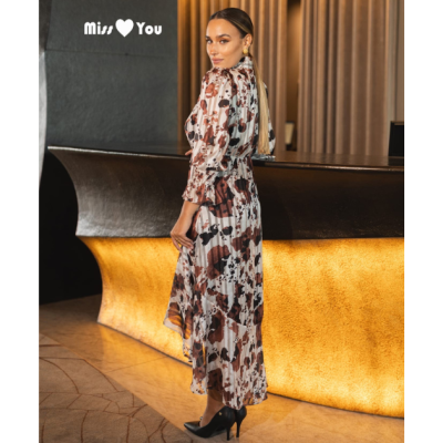 Mulher de vestido midi floral castanho e branco com salto alto preto, em interior com balcão iluminado