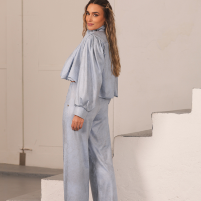 mulher com conjunto azul claro de manga larga e calças largas junto a escadas brancas