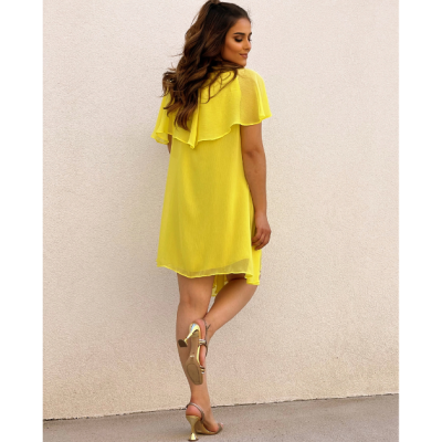 Mulher com vestido amarelo e sandálias douradas junto a parede clara