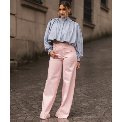 Mulher com calças largas rosa claro e blusa azul clara em ambiente urbano