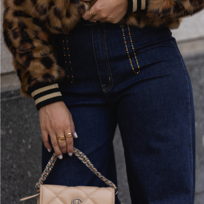 Casaco pele animal castanho, jeans azul escuro com tachas douradas e mala bege com alça de corrente