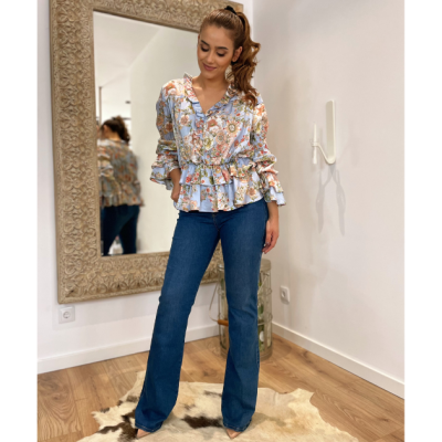 mulher vestindo blusa floral de manga comprida e calças jeans azuis em ambiente interior com espelho e tapete de pele