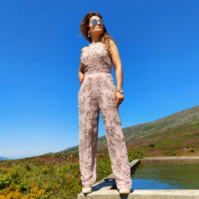 Mulher com macacão rosa claro florido ao ar livre perto de lago e colinas