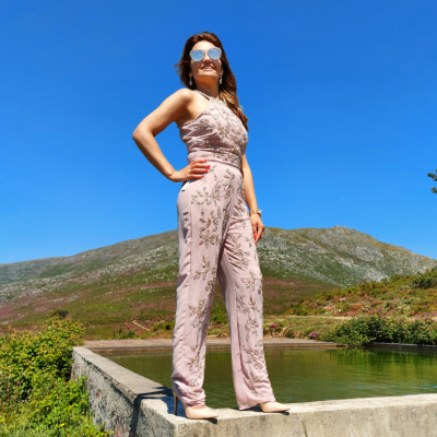 Mulher de macacão bege claro com estampas florais em ambiente de montanha e céu azul