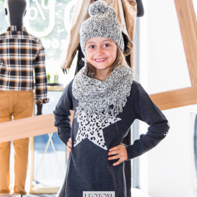 Menina com vestido, cachecol e gorro cinza e branco dentro de loja