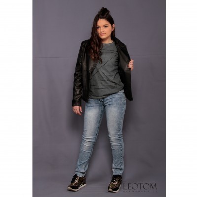 Mulher com casaco preto, camisa cinza, jeans azul claro e ténis pretos posando em fundo cinza.