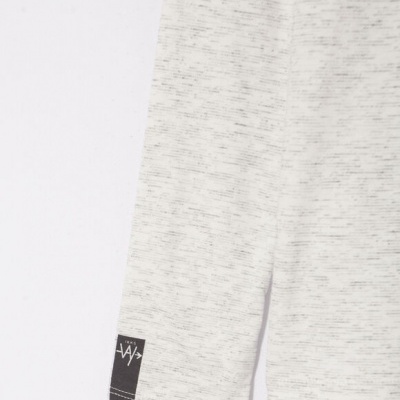 Parte inferior de uma peça de roupa cinzenta clara com etiqueta preta na bainha.