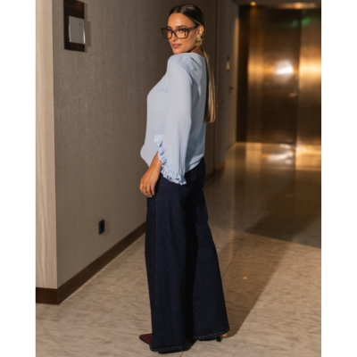 Mulher com blusa azul clara e calças de ganga largas em corredor interior