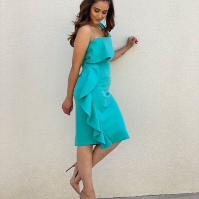 Vestido azul turquesa com babado e laço, sapatos nude, parede branca