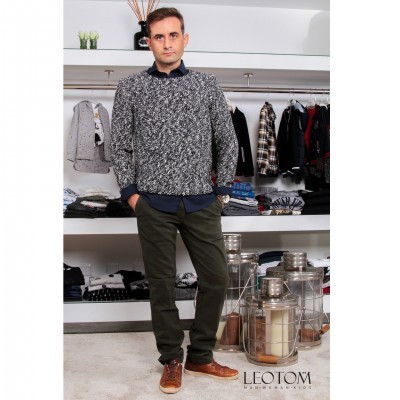 Homem com camisola cinzenta, calças verdes e sapatos castanhos em loja de roupa com lanternas decorativas.