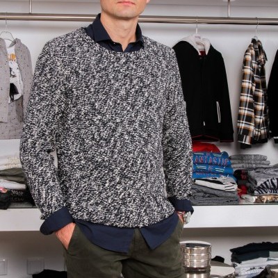 Homem com camisola cinzenta e preta e camisa azul numa loja de roupas