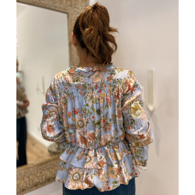 Blusa feminina azul claro com estampa floral, mangas bufantes e babados na bainha vista de costas