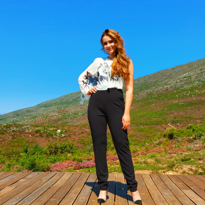 Mulher com blusa branca estampada e calças pretas em plataforma de madeira ao ar livre