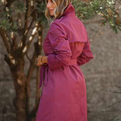 Mulher com casaco rosa magenta ao ar livre junto a árvore e parede cinza