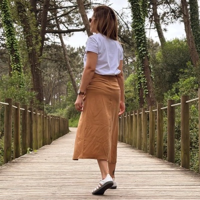 Mulher de costas numa passadeira de madeira com saia castanha e t-shirt branca