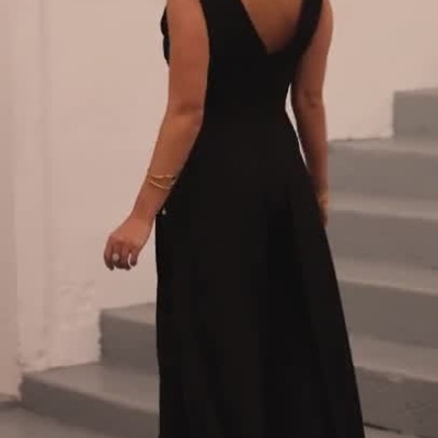 Mulher a usar macacão preto com decote em V posando em escadas cinzentas interiores