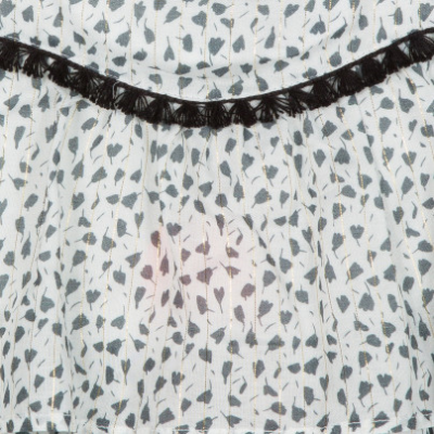 tecido branco com padrão de folhas pretas e faixa decorativa preta com franjas