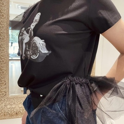 T-shirt preta com estampa branca de menina em cadeira de rodas com saia azul e organza preta franzida.