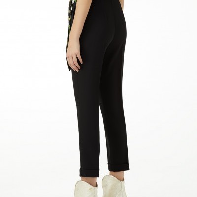 Calças pretas com barra virada e botas brancas de salto em madeira