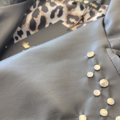 Peça de roupa preta com tachas metálicas e padrão animal com texto