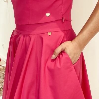 Vestido rosa com saia ampla e bolsos, detalhes de corações dourados