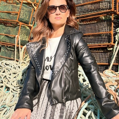 Mulher com casaco preto de pele sintética e óculos escuros sentada sobre redes de pesca e cordas.