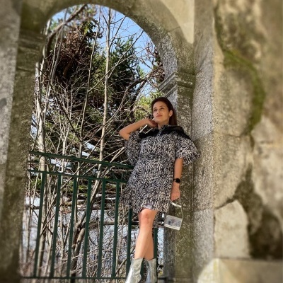 Mulher com vestido animal print e botas prateadas numa varanda de pedra