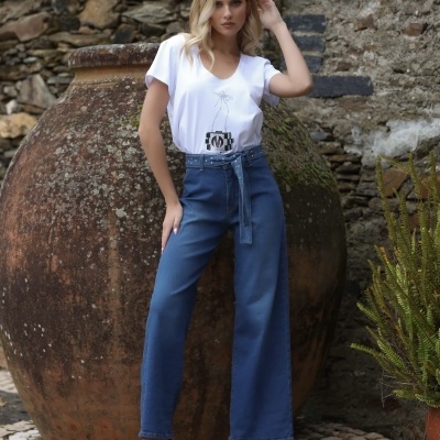 Mulher com t-shirt branca e calças largas azuis posando junto a ânfora grande exterior