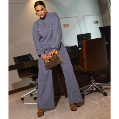 Mulher com fato azul cinzento segurando mala Louis Vuitton castanha numa sala de reuniões