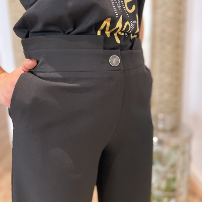 Calças pretas com cintura alta e botão metálico usadas com t-shirt preta com texto dourado