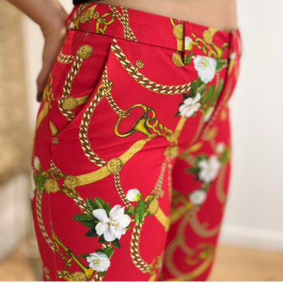 Calças femininas vermelhas com padrão dourado de correntes e flores brancas em ambiente interno