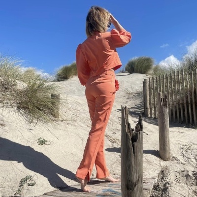 Conjunto feminino laranja em praia com areia e vegetação