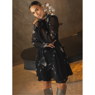 Mulher com vestido preto floral e botas prateadas num ambiente interior neutro