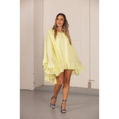 Vestido amarelo claro com bainha assimétrica e folhos, usado por mulher com sandálias azuis em ambiente interno.