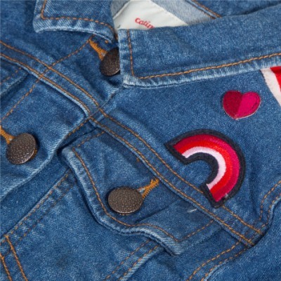 Detalhe de roupa de ganga azul com bordados de arco-íris e coração vermelho