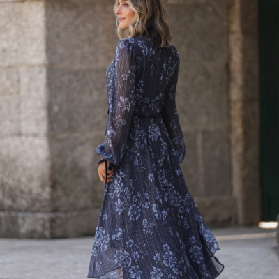 Vestido midi azul floral com mangas compridas usado por mulher em ambiente exterior de pedra.