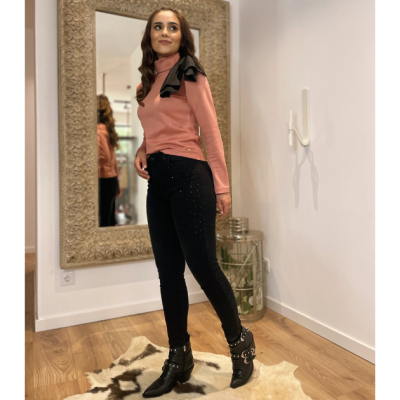 Mulher vestindo t-shirt rosa com laço preto, calças pretas justas e botins pretos com fivelas