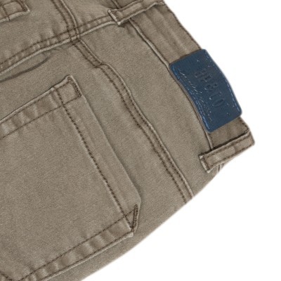 Calças castanhas com etiqueta azul no cós e bolso traseiro direito visível