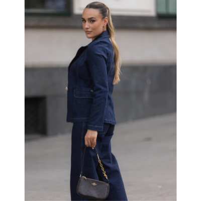 Mulher com fato de ganga azul escuro e mala de mão castanha escura com alça dourada