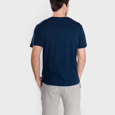 Homem de costas com t-shirt azul escura e calções cinza claros.