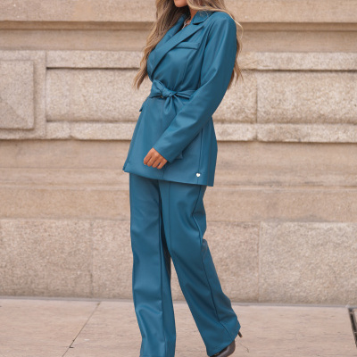 Mulher a usar conjunto azul-acinzentado com blusão com cinto e calças e sapatos de salto castanhos