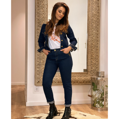 Mulher em casaco e jeans azul escuro com botas pretas em frente a espelho com moldura trabalhada